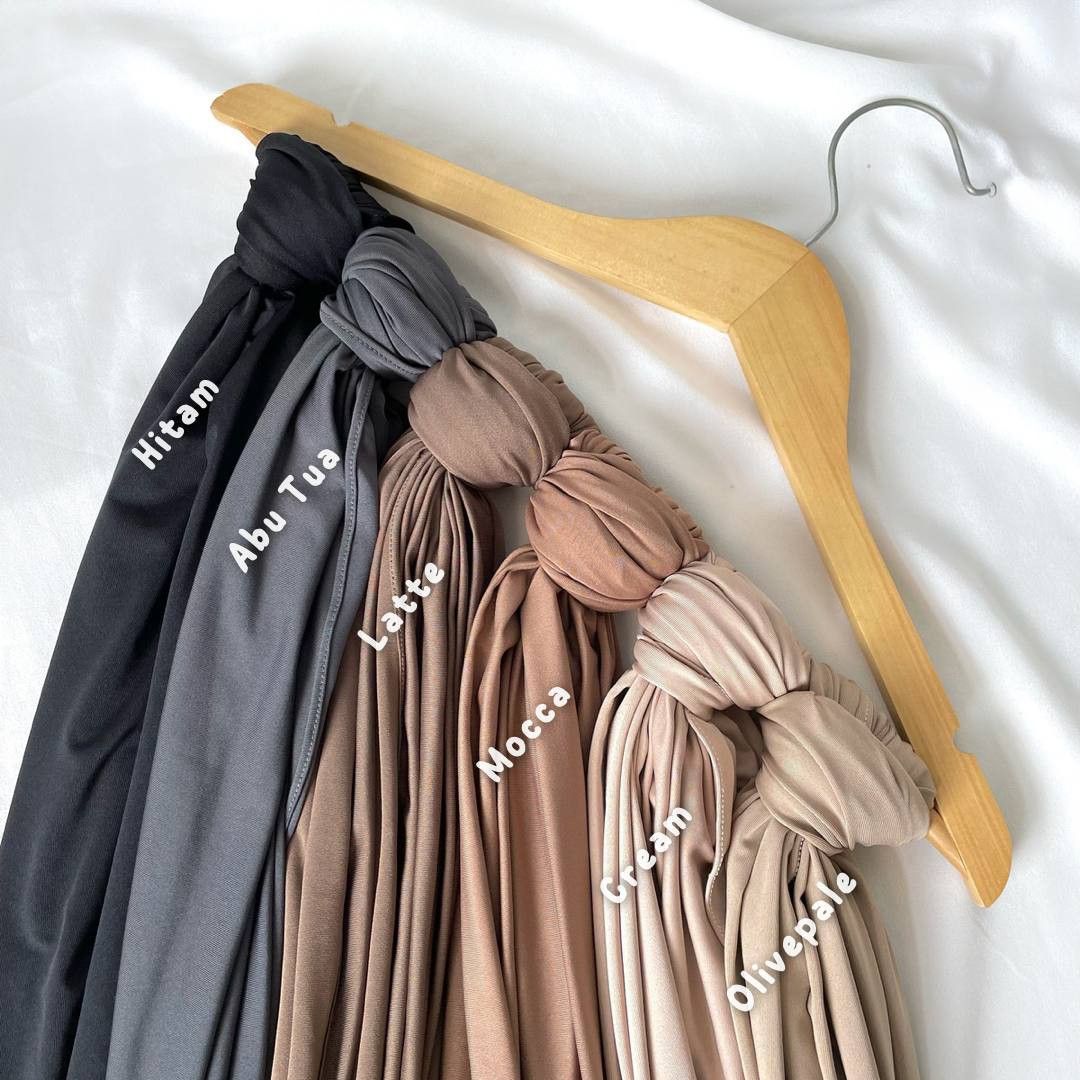 Hijab pasmina premium warna pastel dengan detail bordir emas disimpan rapi di atas meja